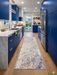 2.8' x 8' runner ivory gray & blue marble swirl abstract modern area rug placed in a contemporary kitchen with blue cabinetry, marble countertops, and wood flooring.