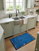 2' x 3' Rectangular Blue Multicolor Border Modern Washable Area Rug placed in a bright kitchen in front of a farmhouse sink and sage green cabinets.