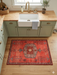 2' x 3' Rectangular Coral Red Tribal Medallion Traditional Washable Area Rug placed in a kitchen in front of a farmhouse sink with warm cabinetry and soft natural light.