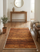 2' x 3' Rectangular Rust Gold Distressed Abstract Modern Washable Area Rug placed in a modern entryway with a wooden console table, round mirror, and natural decor.
