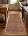 2' x 4' Rectangular Rust Orange & Beige Solid Textured Modern Washable Area Rug styled in a warm contemporary kitchen between wooden cabinets.