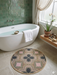 3' Round Pink Green Geometric Bohemian Washable Area Rug placed in a spa-inspired bathroom beside a freestanding tub with green tile walls and natural decor.
