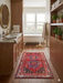 3' x 5' Rectangular Red & Blue Tribal Geometric Southwestern Washable Area Rug placed in a rustic bathroom with wood cabinetry and a freestanding clawfoot tub.