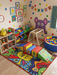 3' x 5' rectangular multicolor cartoon abstract kids playful area rug placed in a bright playroom with toy storage, soft play blocks, and a ball pit.