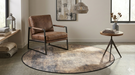 4' Round Beige & Brown Distressed Modern Abstract Area Rug styled in a cozy living room seating area with leather chair and side table.