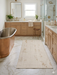 4' x 6' Rectangular Ivory & Gold Distressed Abstract Modern Washable Area Rug styled in a luxurious bathroom beside a freestanding copper bathtub.