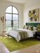 5' x 7' Rectangular Mustard Gold Distressed Medallion Traditional Washable Area Rug placed under a bed in a bright contemporary bedroom with green accents and large arched windows.
