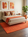 5' x 7' Rectangular Orange Rust Solid Minimalist Modern Area Rug styled in a bedroom with neutral bedding and coordinated accent pillows.