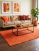 5' x 7' Rectangular Orange Rust Solid Minimalist Modern Area Rug styled in a living room with warm-toned decor and abstract wall art.