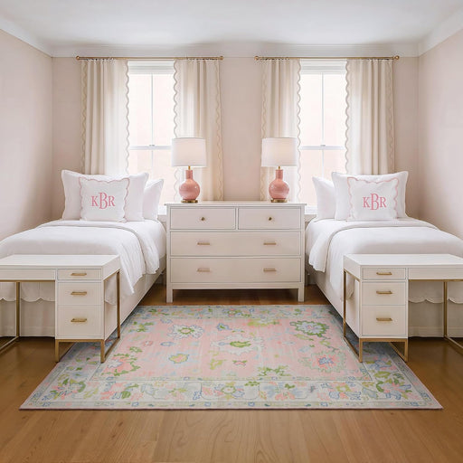 5' x 7' Rectangular Pink Multicolor Floral Traditional Washable Area Rug placed in a charming girls’ bedroom between two twin beds with pink monogram pillows and white furniture.