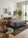 5' x 8' Rectangular Black Multi Color Distressed Ornate Vintage Traditional Area Rug styled in a bedroom.