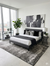 5' x 8' Rectangular Charcoal Ivory Distressed Abstract Modern Area Rug placed under a modern bed in a minimalist bedroom with gray and white bedding.