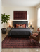 5' x 8' rectangular burgundy & black distressed tribal traditional area rug placed in a bedroom with a dark upholstered bed and warm accent pillows.