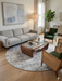 6' Round Beige & Gray Distressed Abstract Modern Area Rug styled in a living room with modern furniture and warm wood accents.
