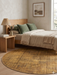 6' Round Gold & Brown Distressed Abstract Modern Washable Area Rug styled in a bedroom with warm wood furniture and neutral bedding.