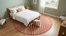6' Round Red Ivory Striped Modern Contemporary Area Rug placed in a bedroom beneath the bed, adding a warm modern accent to the space.
