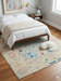 6' x 6' Square Ivory & Blue Tribal Medallion Traditional Area Rug placed in a bedroom beneath a bed with neutral bedding.