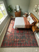 6' x 6' square red & charcoal tribal geometric southwestern area rug styled in a cozy bedroom with warm wood furniture and neutral accents.