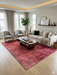 6' x 9' Rectangular Red & Pink Distressed Abstract Modern Area Rug styled in a living room with a sofa, accent chairs, and large windows.