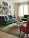6' x 9' rectangular olive green & multicolor floral medallion traditional area rug placed in a vibrant living room with a teal sofa, accent chairs, and colorful wall art.