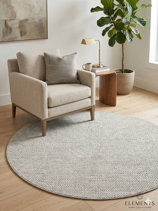 7' round ivory gray micro dot textured modern area rug placed in a cozy reading corner with a neutral armchair, wood side table, and indoor plant.