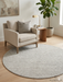 7' round ivory gray micro dot textured modern area rug placed in a cozy reading corner with a neutral armchair, wood side table, and indoor plant.