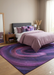 7' x 10' Rectangular Purple & Pink Abstract Modern Area Rug placed beneath a bed in a chic modern bedroom.