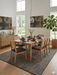 7' x 10' rectangular beige & charcoal textured minimalist modern area rug placed in a dining room with a wooden table, woven chairs, and natural light.