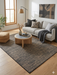7' x 10' rectangular beige & charcoal textured minimalist modern area rug placed in a living space with modern wall art, indoor plants, and clean-lined furniture.