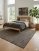 7' x 10' rectangular beige & charcoal textured minimalist modern area rug styled in a bedroom with a low-profile bed, neutral bedding, and warm wood accents.