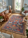 7' x 9' Rectangle Charcoal Gray & Rust Folk Tribal Washable Area Rug placed in a cozy living room with leather sofa, accent chair, and wooden coffee table.