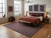7' x 9' Rectangular Charcoal Rust Geometric Tribal Traditional Washable Area Rug placed under a bed in a contemporary bedroom with rich rust bedding and dark wood furniture.