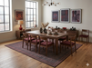 7' x 9' Rectangular Charcoal Rust Geometric Tribal Traditional Washable Area Rug shown beneath a wooden dining table with upholstered chairs in a modern dining room with warm earth-tone décor.