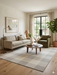 7' x 9' Rectangular Ivory & Gray Checkered Plaid Modern Farmhouse Area Rug placed in a cozy living room with a sofa, accent chair, and round coffee table.