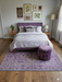 7' x 9' Rectangular Ivory & Purple Floral Medallion Traditional Area Rug styled in a serene bedroom with a lavender upholstered bed and soft neutral bedding.