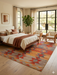 7' x 9' Rectangular Orange Multi Color Geometric Tribal Southwestern Area Rug styled in a bedroom with neutral bedding and purple accents.