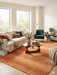 7' x 9' Rectangular Orange Terracotta Distressed Solid Modern Area Rug styled in a living room with a sofa, accent chair, and modern decor.