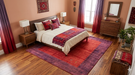 7' x 9' Rectangular Red & Purple Solid Border Contemporary Area Rug placed beneath a bed in a cozy bedroom.