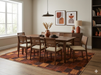 7' x 9' Rectangular Rust Gold Checkered Geometric Modern Washable Area Rug shown beneath a wooden dining table with woven-back chairs in a warm contemporary dining room.