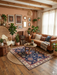 7' x 9' rectangular navy blue & red floral medallion traditional area rug placed in a warm boho living room with a leather sofa, woven accents, plants, and wood flooring.