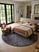 8' Round Charcoal Gray Textured Abstract Modern Washable Area Rug styled in a bedroom with a bed and accent chair.
