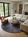 8' Round Charcoal Gray Textured Abstract Modern Washable Area Rug styled in a living room with a sectional sofa and coffee table.