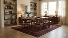 8' x 10' rectangular burgundy & black distressed geometric traditional area rug placed in a dining room with a wood table, matching chairs, and warm ambient lighting.