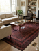8' x 10' rectangular burgundy & black distressed geometric traditional area rug placed in a living room with a neutral sofa, wood coffee table, and built-in shelving.