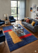 8' x 12' Rectangular Blue & Multicolor Abstract Modern Area Rug styled in a contemporary living room with sofa, armchairs, and glass coffee table.