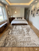 8' x 12' Rectangular Olive Green & Cream Distressed Abstract Modern Area Rug placed in a bedroom with a platform bed, neutral bedding, and natural light from large windows.