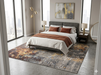 8' x 8' Square Gray Gold Abstract Modern Washable Area Rug placed in a modern bedroom with a gray upholstered bed, white bedding, and rust-colored accent pillows.